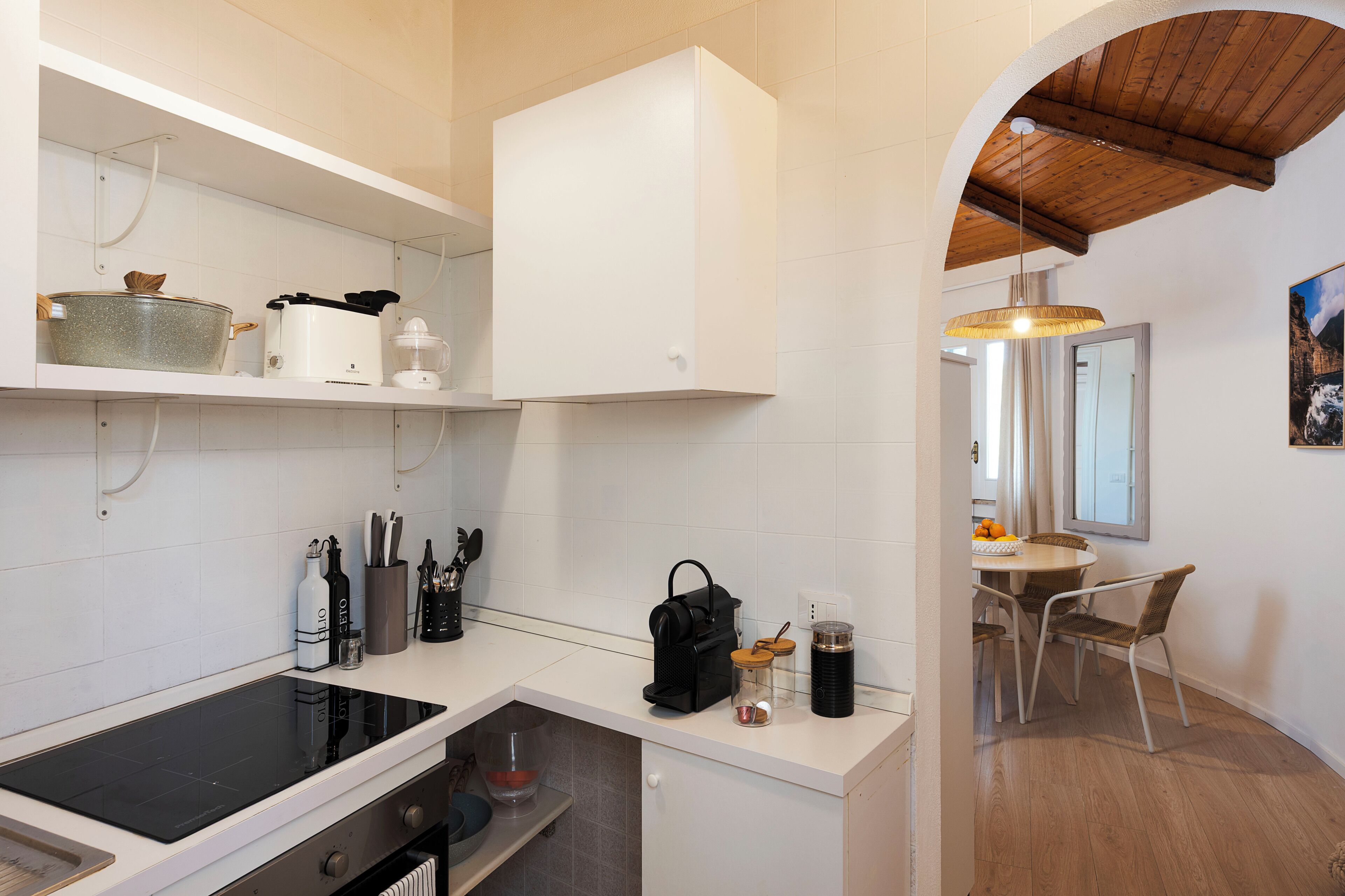 A modern kitchen with white cabinetry, a built-in stove, and a dining area with a table and chairs.