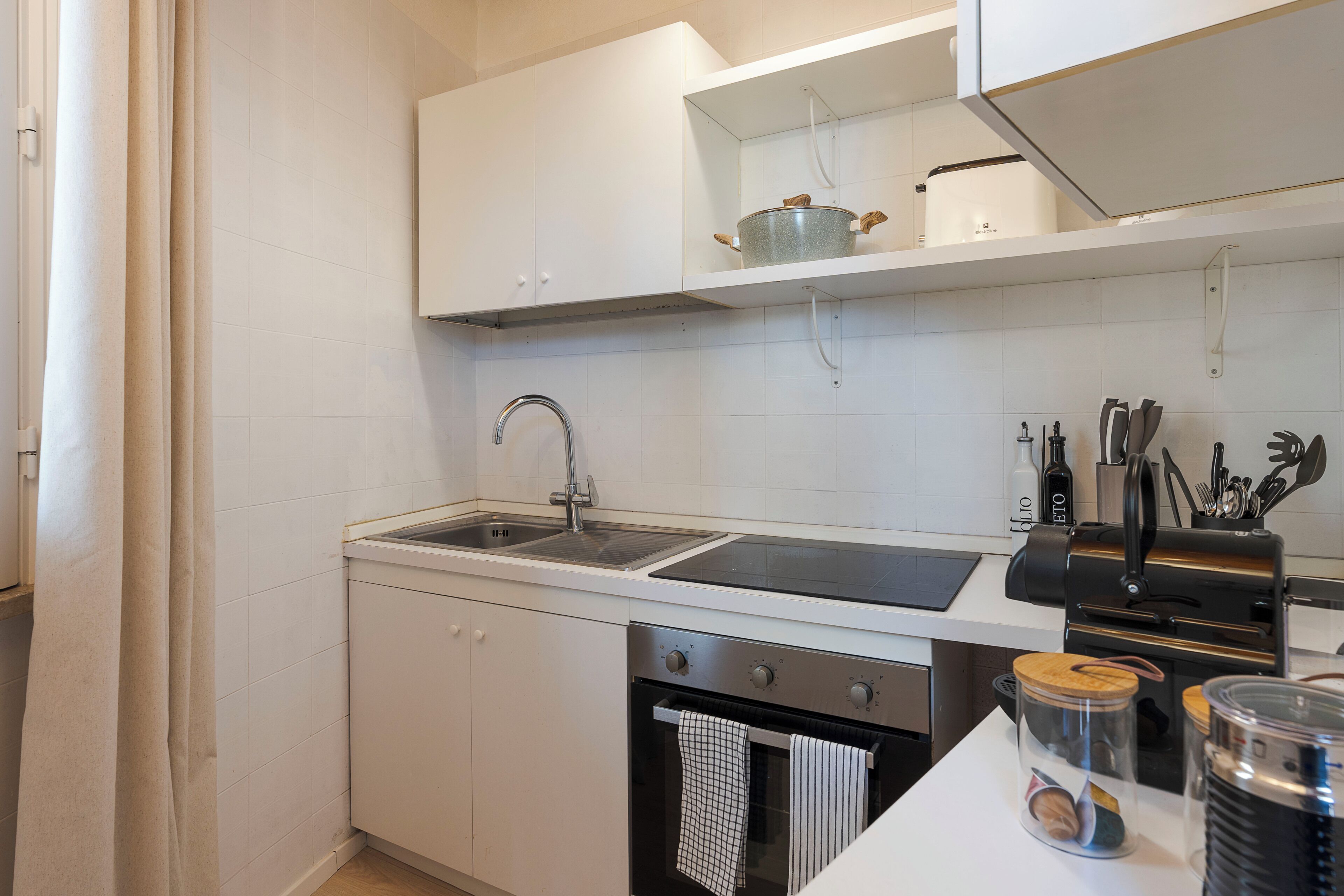 A modern kitchen with white cabinetry, a stainless steel sink, and a built-in oven.
