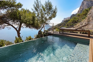 Una piscina infinita con terraza de madera, con vista a una costa montañosa.