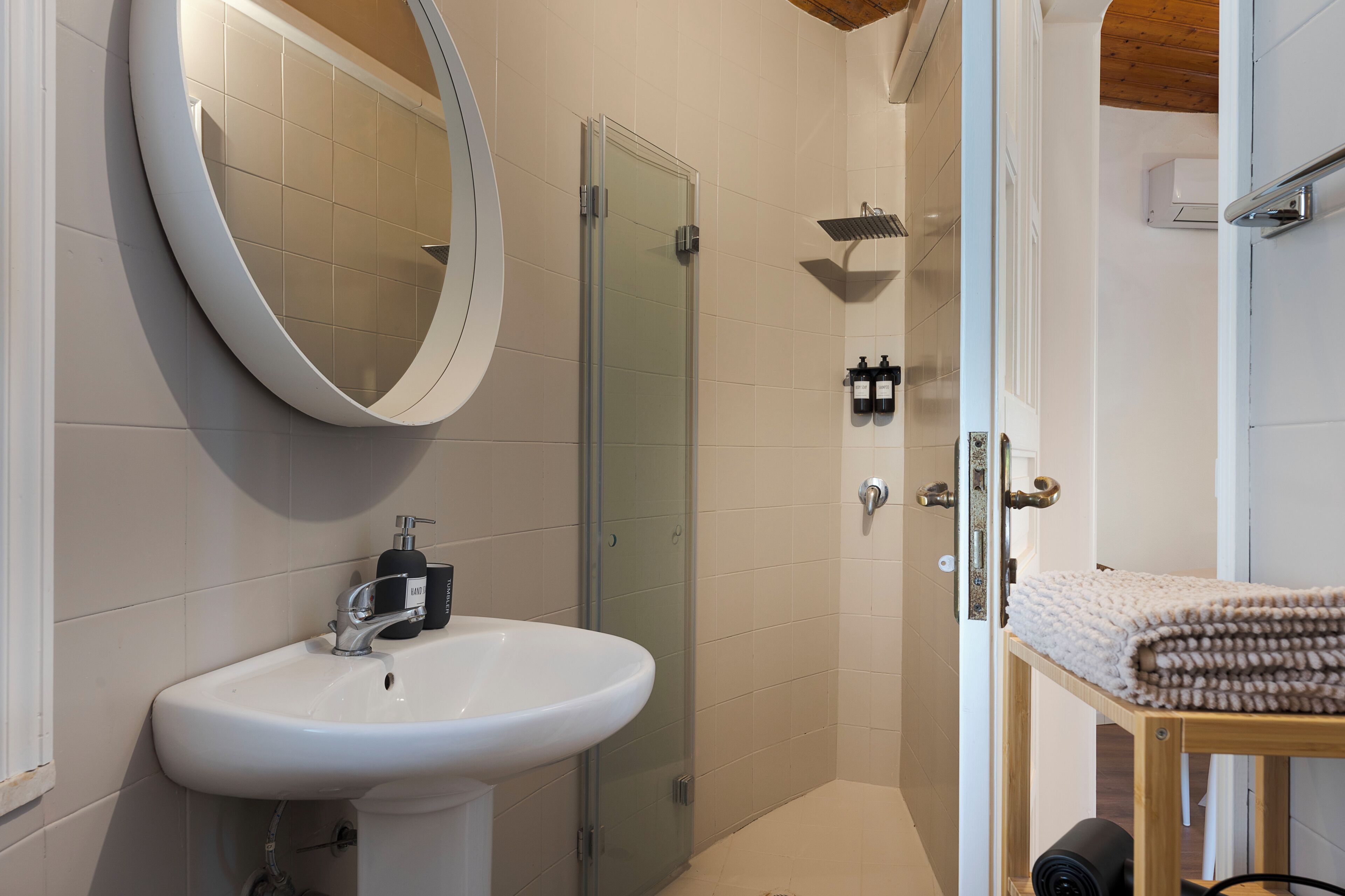 Un baño moderno con un lavamanos blanco, un espejo, cabina de ducha de vidrio y un perchero para toallas.