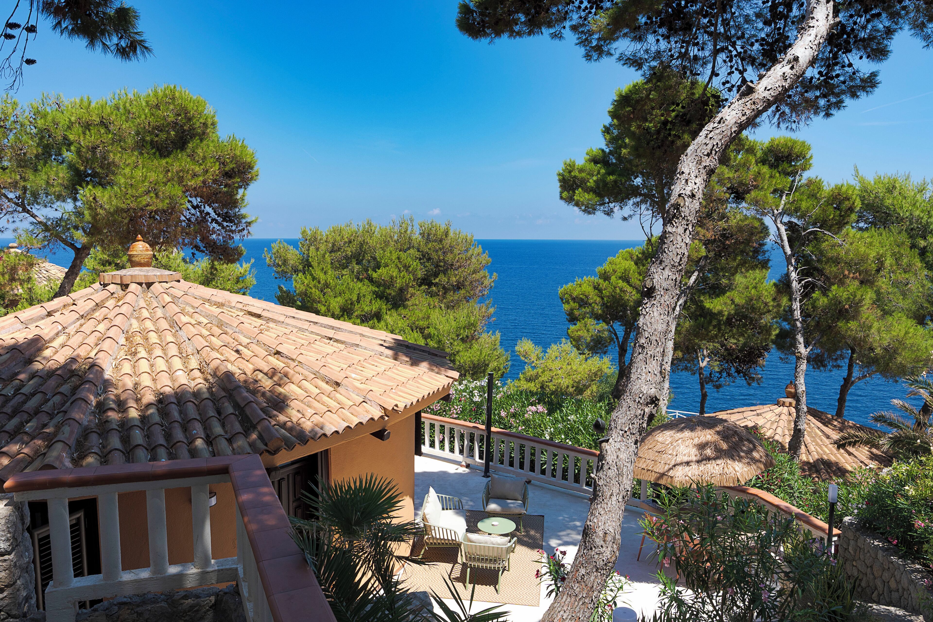 A coastal property with a terrace overlooking the sea, surrounded by pine trees.