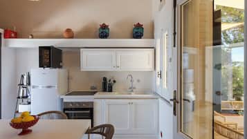 A compact kitchen with white cabinetry, a built-in stove, and a dining area with a wicker chair.