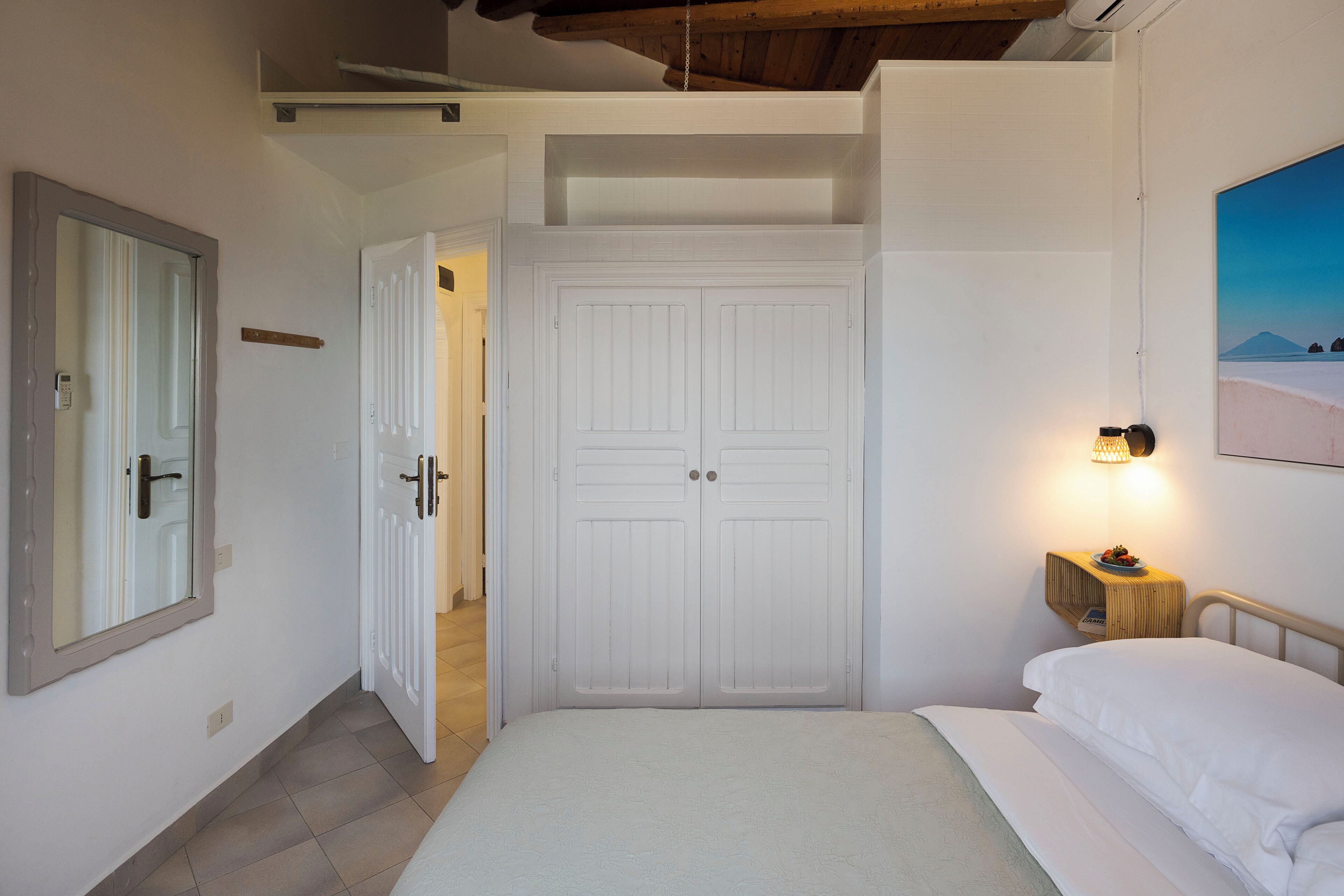 Una camera da letto con un letto, un armadio, un comodino con una lampada e un quadro appeso al muro.
