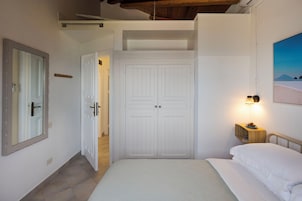 Un dormitorio con cama, armario, mesita de noche con lámpara y un cuadro en la pared.