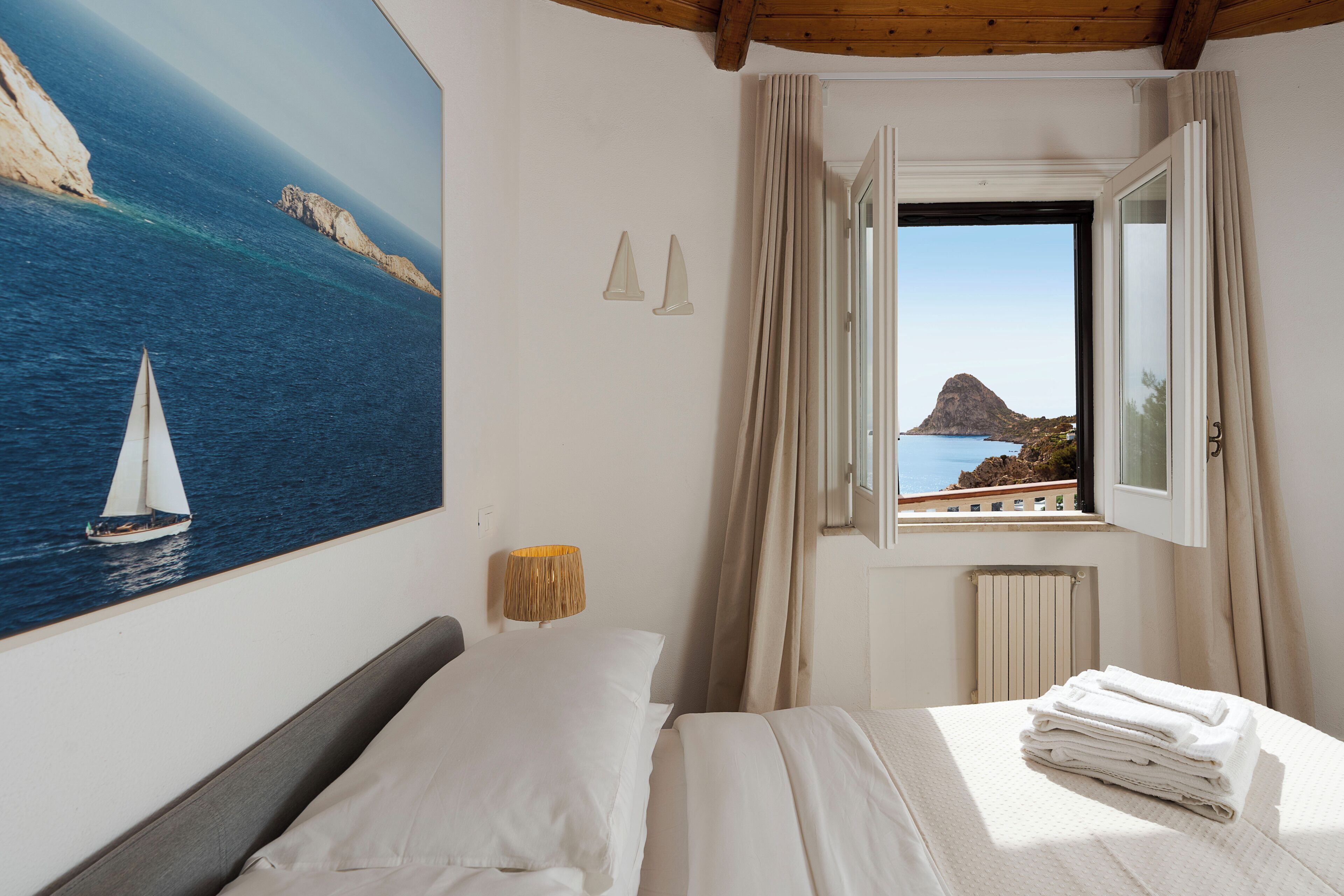 Un dormitorio con cama, ventana con cortinas, un cuadro de un velero y un radiador.
