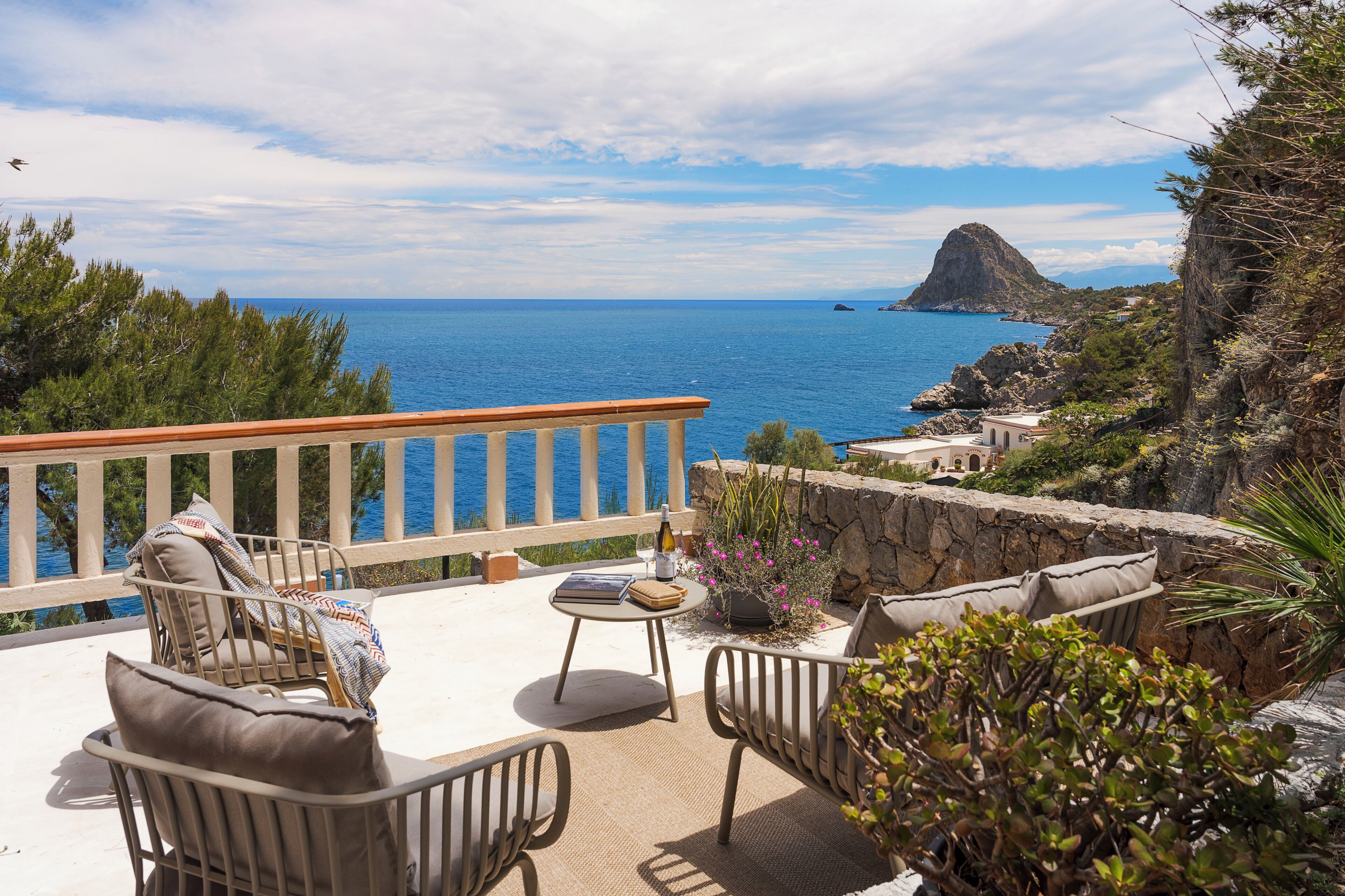 A terrace with outdoor furniture, a view of the sea, and a rocky landscape.