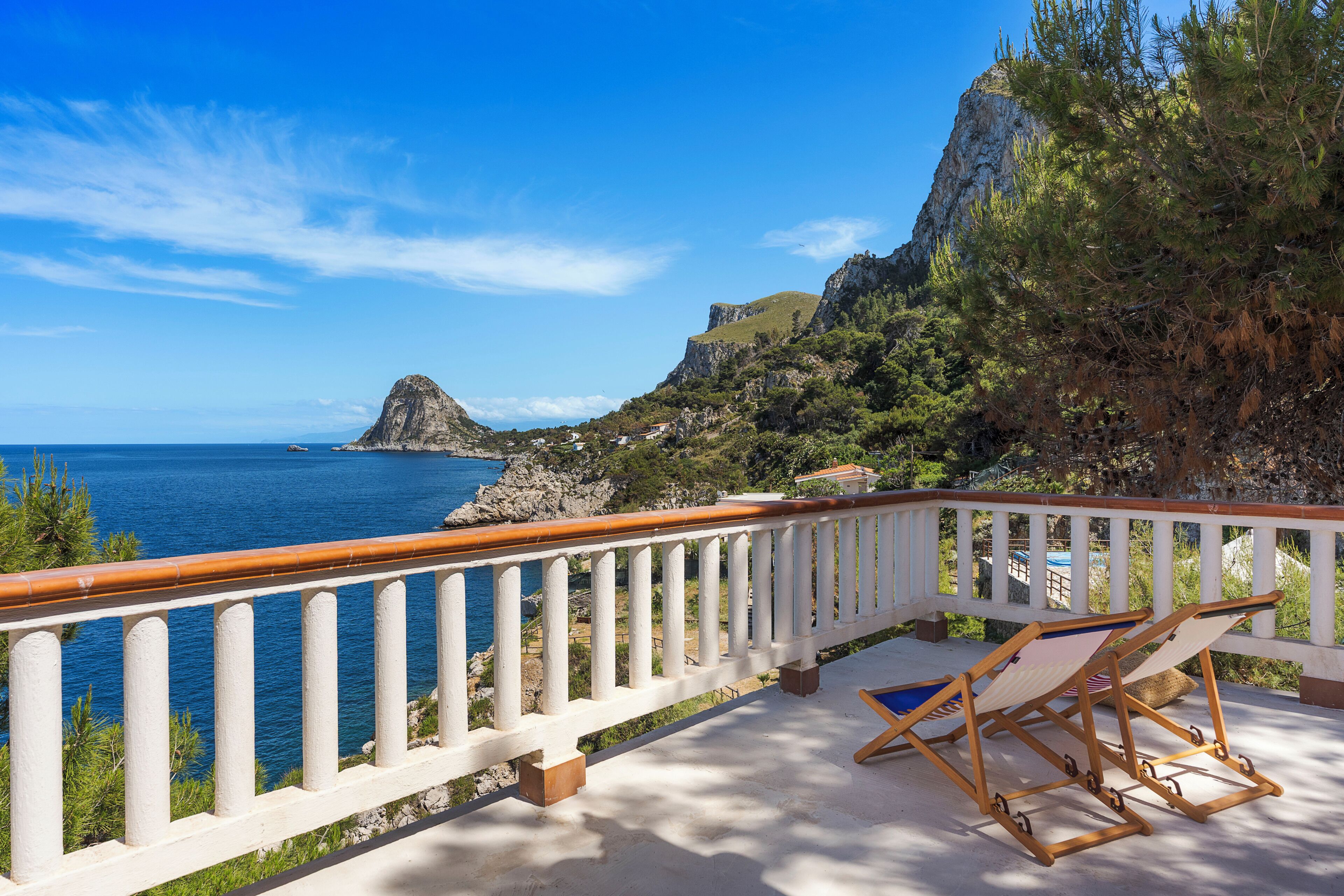 A balcony with a white railing overlooking a coastal landscape with a clear sky.