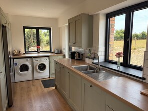 A modern kitchen with a built-in washing machine, a large window with a view of the outdoors, and a sink with a faucet. - High View Barn (Launceston)
