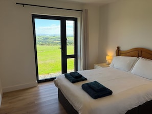 Habitació d'hotel amb un llit gran, una petita taula de nit amb una làmpada i una porta corredissa de vidre que dona a una zona exterior enjardinada.