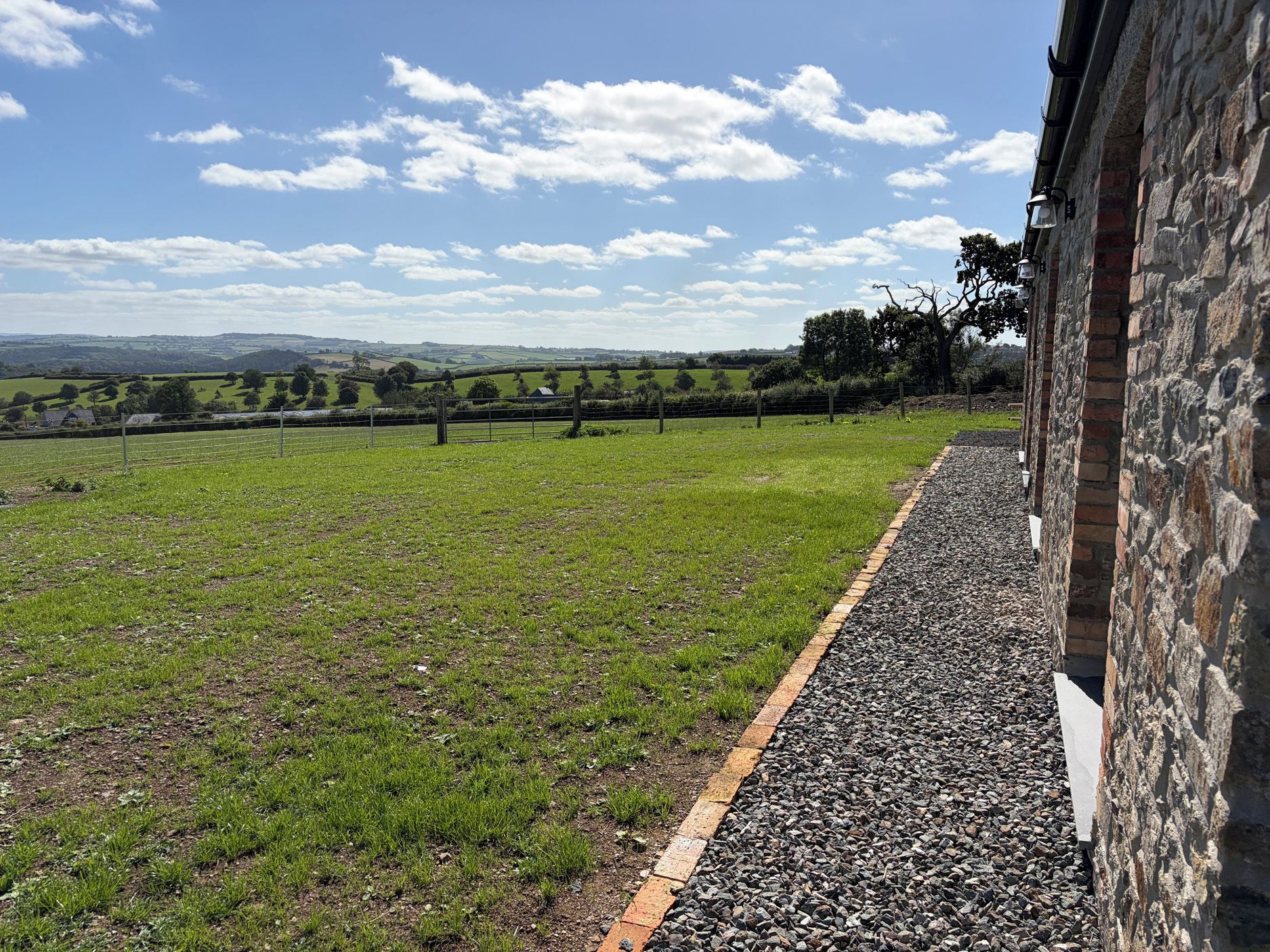 A view of a grassy field with a stone wall and a building on the right.