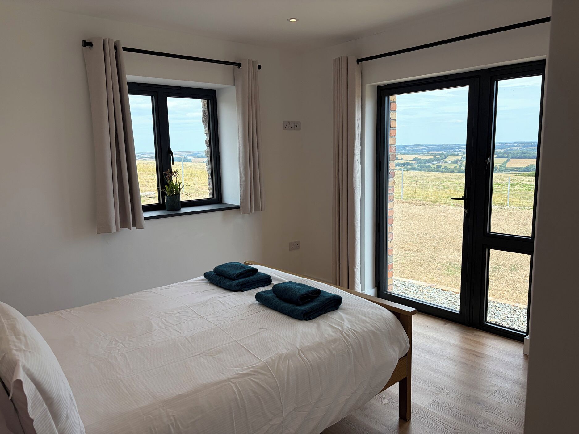 A bedroom with a bed, two towels, a window with curtains, and a view of the countryside.