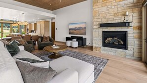 A spacious living room with a stone fireplace, a dining area, and a view of the outdoors. - Clubhouse Close Villa, golf, min 90 day stay (Heber City)
