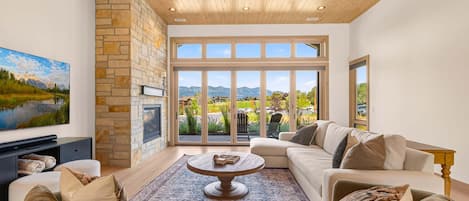 A spacious living room with a stone fireplace, large windows, and a view of a mountainous landscape.