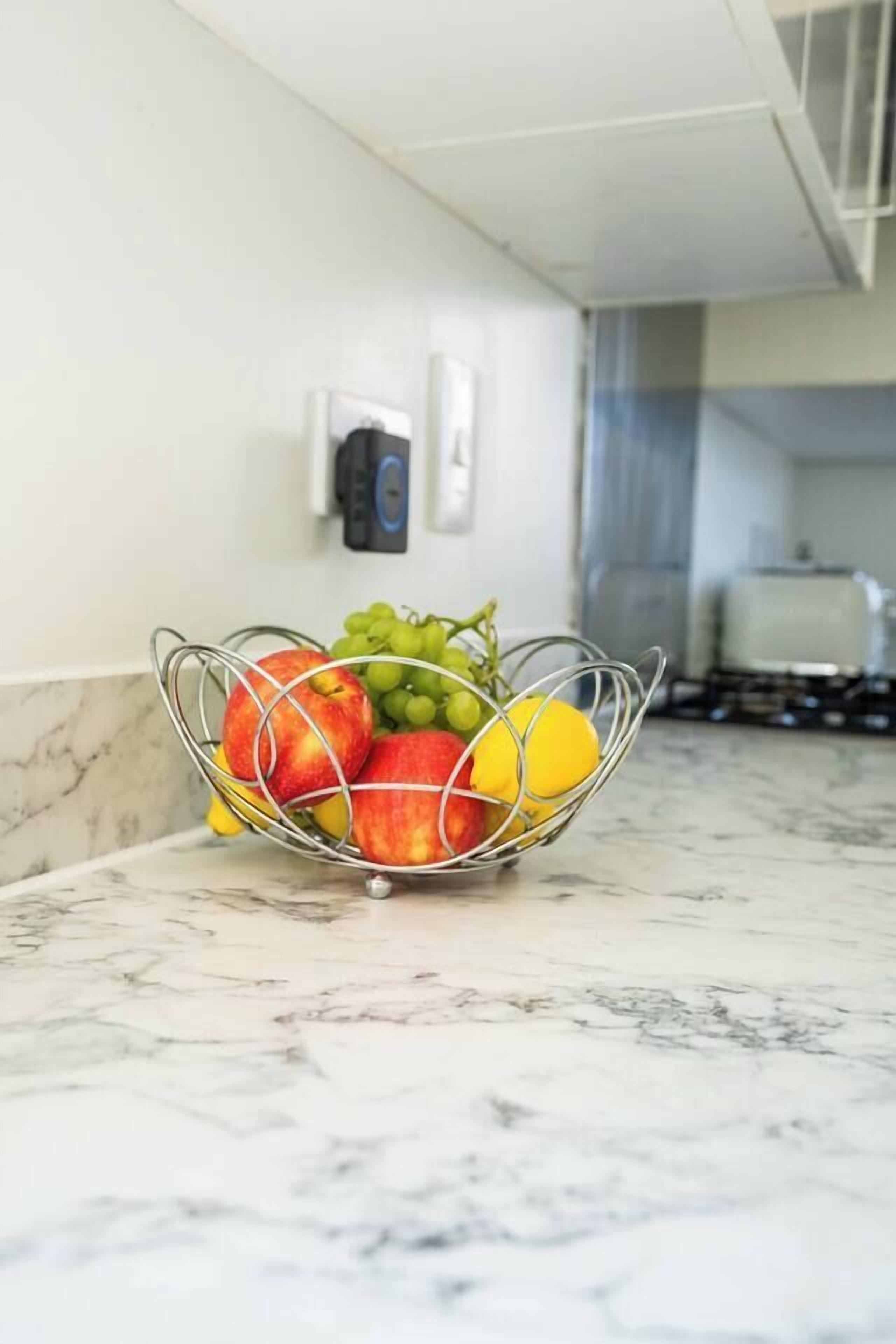A kitchen counter with a fruit bowl containing apples, grapes, and a lemon.