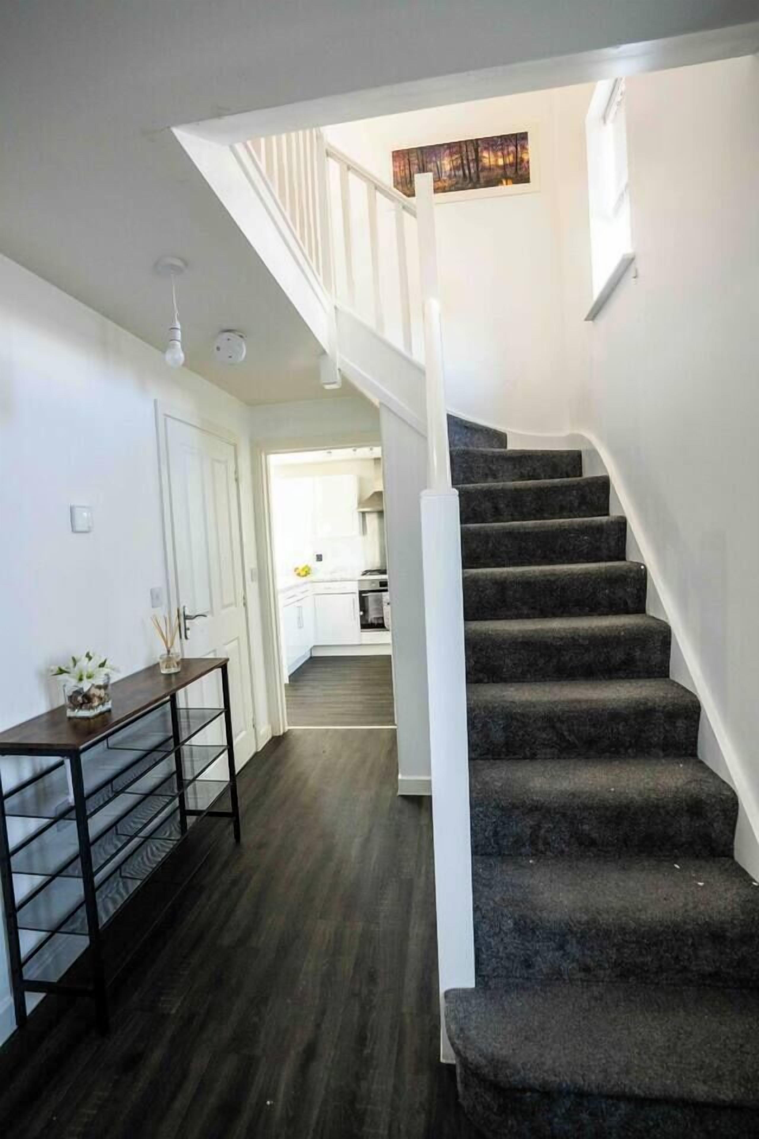 A staircase leading to a second floor with a dark carpeted floor and white walls.
