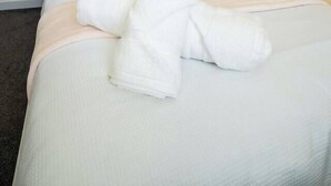 Ein ordentlich bezogenes Bett mit einer weißen Daunendecke und einem gefalteten weißen Handtuch.