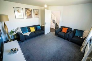 A living room with two sofas, a coffee table, and a lamp. There is a staircase leading to another level. - 3-Bed Serviced Home | Ensuite | Work Desk| Bilston (West Midlands)