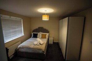 Quarto com cama, mesas de cabeceira, guarda-roupa e janela com persianas.