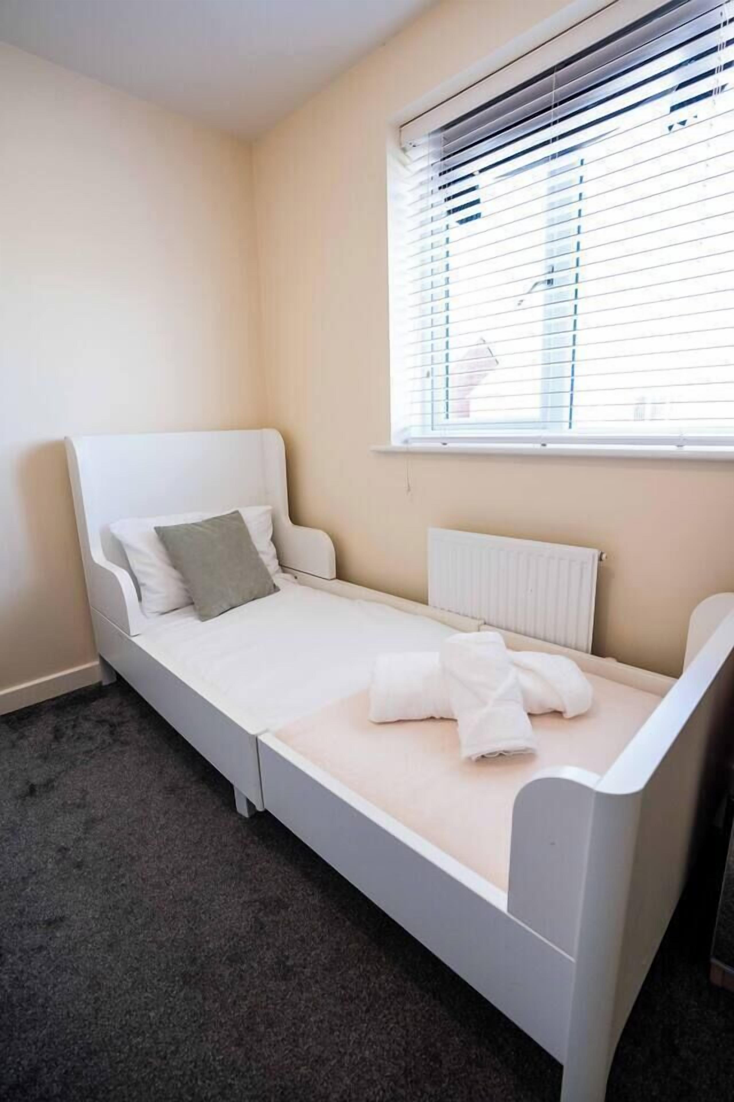 Ein Einzelbett mit weißem Gestell, einem grauen Kopfkissen und einer weißen Decke.