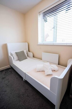 A single bed with a white frame, a grey pillow, and a white blanket. - 3-Bed Serviced Home | Ensuite | Work Desk| Bilston (West Midlands)