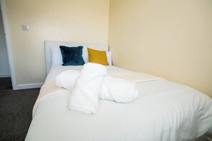 A neatly made bed with white bedding and a folded towel. - 3-Bed Serviced Home | Ensuite | Work Desk| Bilston (West Midlands)