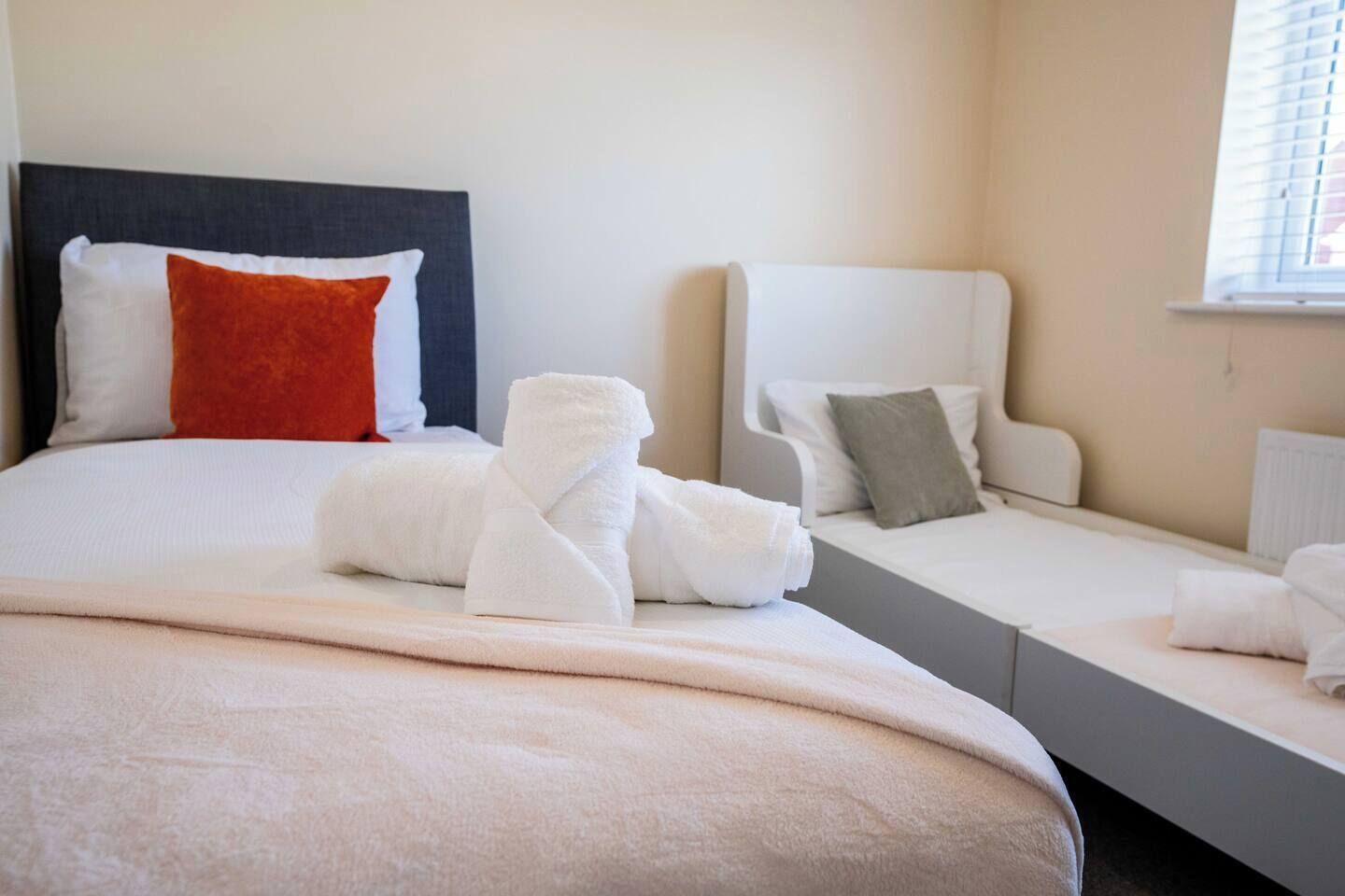 Une chambre d’hôtel avec un grand lit, deux petits lits et une fenêtre avec des stores.