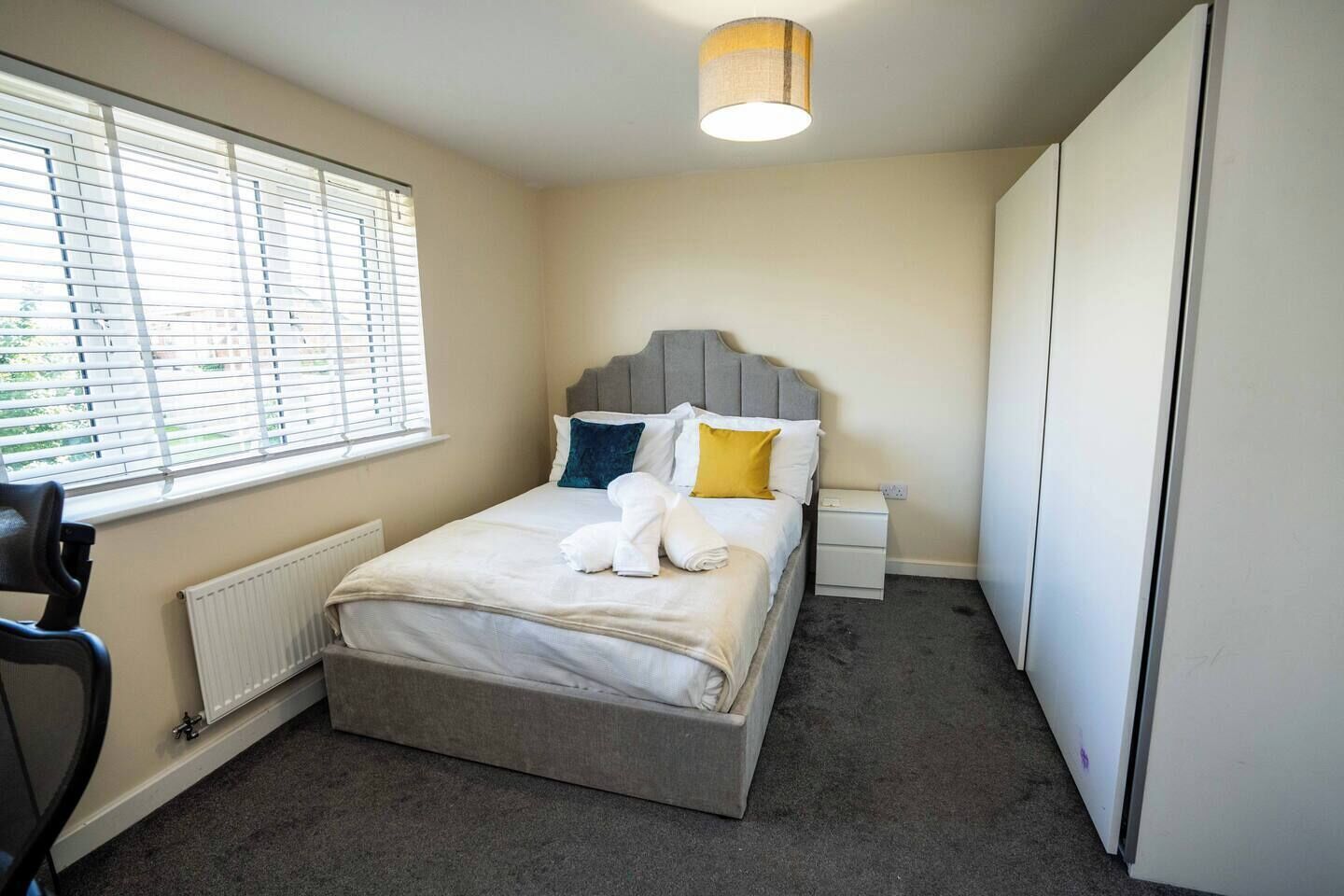 A bedroom with a bed, a nightstand, a radiator, a window with blinds, and a wardrobe.