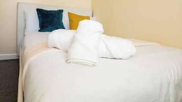 A neatly made bed with a white comforter and pillows, a headboard, and a plain wall.