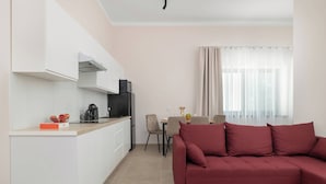 Eine moderne Küche mit weißen Schränken, einem schwarzen Kühlschrank und einer Kaffeemaschine. Es gibt einen Essbereich mit Tisch und Stühlen, und ein rotes Sofa im Wohnzimmer.