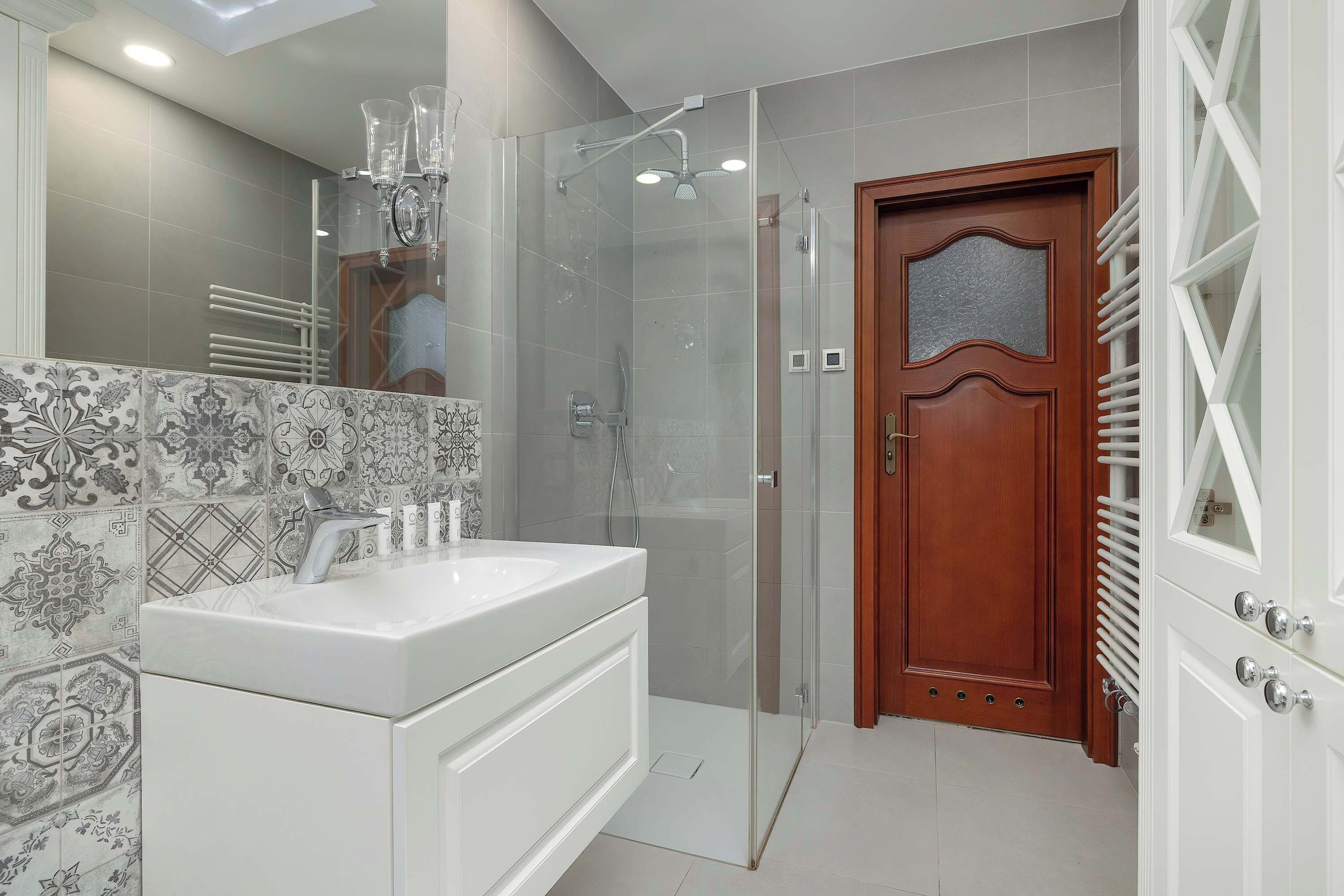 Une salle de bain moderne avec une douche à l’italienne en verre, un lavabo blanc agrémenté d’un pare-éclaboussures décoratif et une porte en bois avec un panneau en verre dépoli.