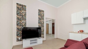 A modern living room with a flat-screen TV, a red sofa, and a kitchen area with cabinets and a countertop. - Charming Studio for 4 | Cosiness and Comfort (Bielsko-Biała)