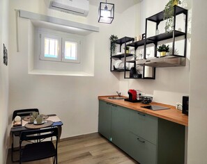 Eine kompakte Küche mit Fenster, ein Essbereich mit Tisch und Stühlen sowie eine eingebaute Regaleinheit mit Dekoration.