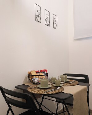 Un comedor con una mesa dispuesta para dos, sillas, una cesta de pan y una pared con tres cuadros enmarcados.