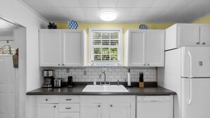 Una cocina con armarios blancos, una ventana con persianas, un lavamanos y un refrigerador.