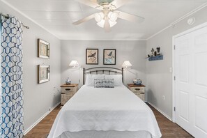 A bedroom with a bed, two bedside tables, a ceiling fan, and wall-mounted artwork.