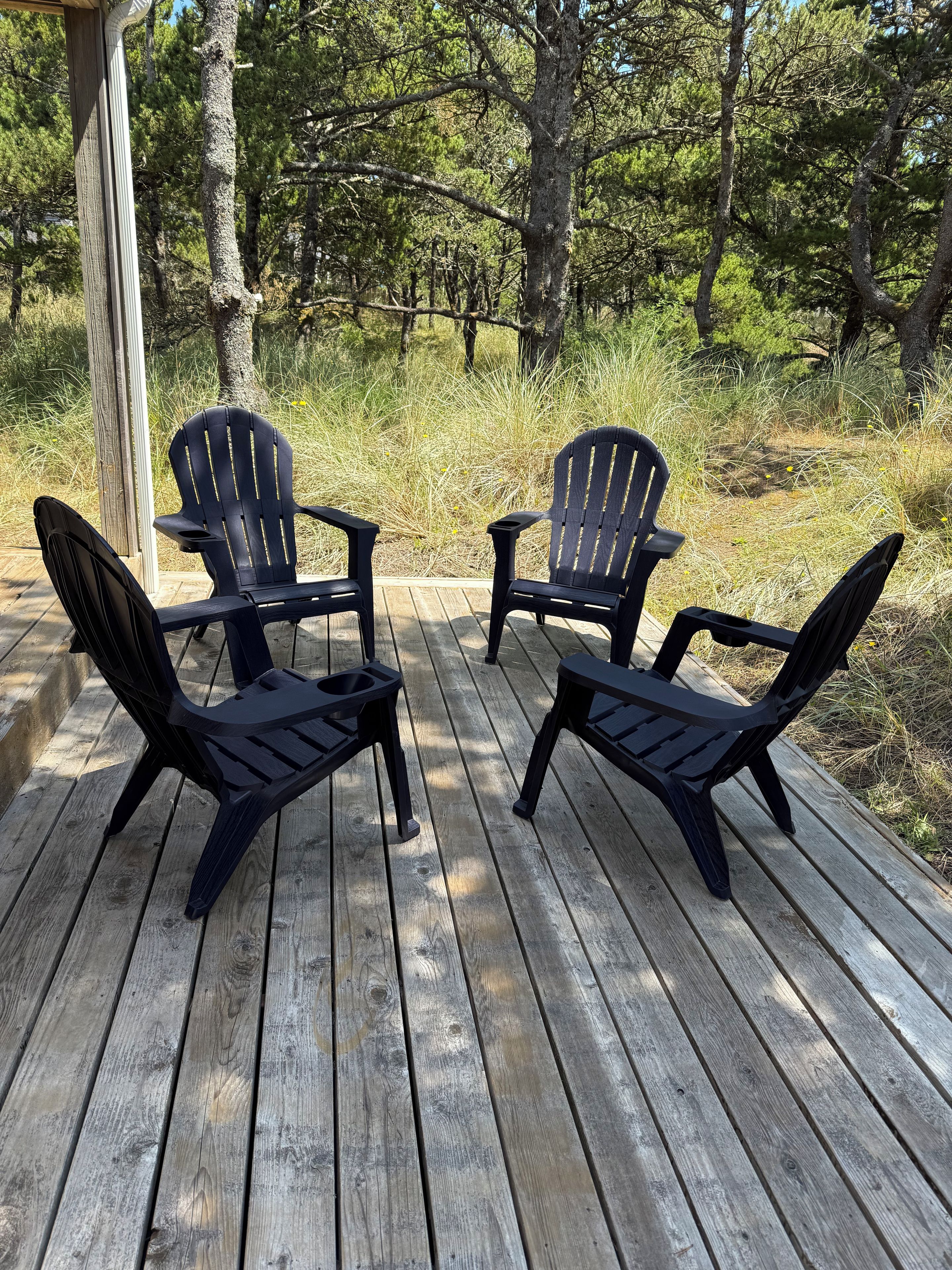A wooden deck with four black Adirondack chairs arranged in a semi-circle.
