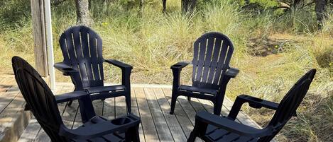A wooden deck with four black Adirondack chairs arranged in a semi-circle.