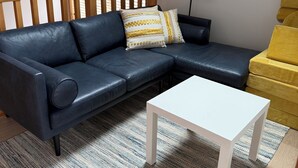 Een moderne woonkamer met een donker leren bank, een witte salontafel en een kamerbreed tapijt met een patroon.