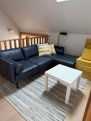 A modern living room with a dark leather sofa, a white coffee table, and a patterned rug. - 3 Min to Sand | Family Fun + Bunk Room | Sleeps 9 (Cloverdale)