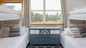 Een slaapkamer met twee stapelbedden, een dressoir met lades en een raam voorzien van gordijnen.