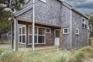 Ein zweistöckiges Haus mit verdeckter Veranda, großen Fenstern und einer Tür.