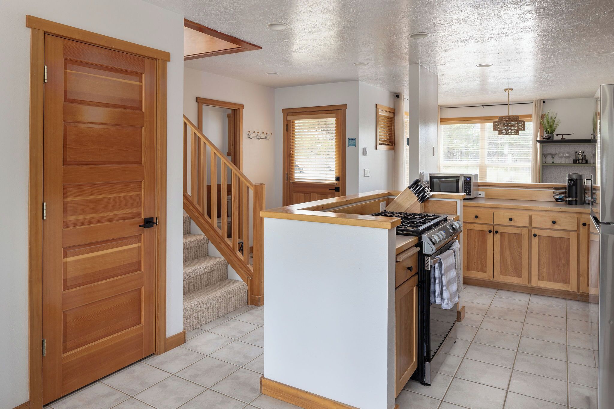 A kitchen with a gas stove, microwave, and refrigerator. There is a wooden staircase leading to another room.