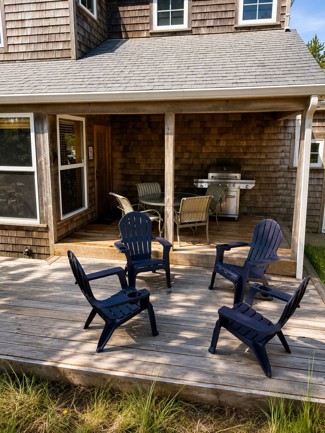 A covered patio with Adirondack chairs and a grill.