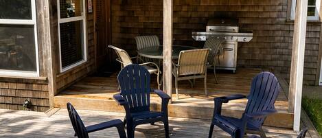 A covered patio with Adirondack chairs and a grill.