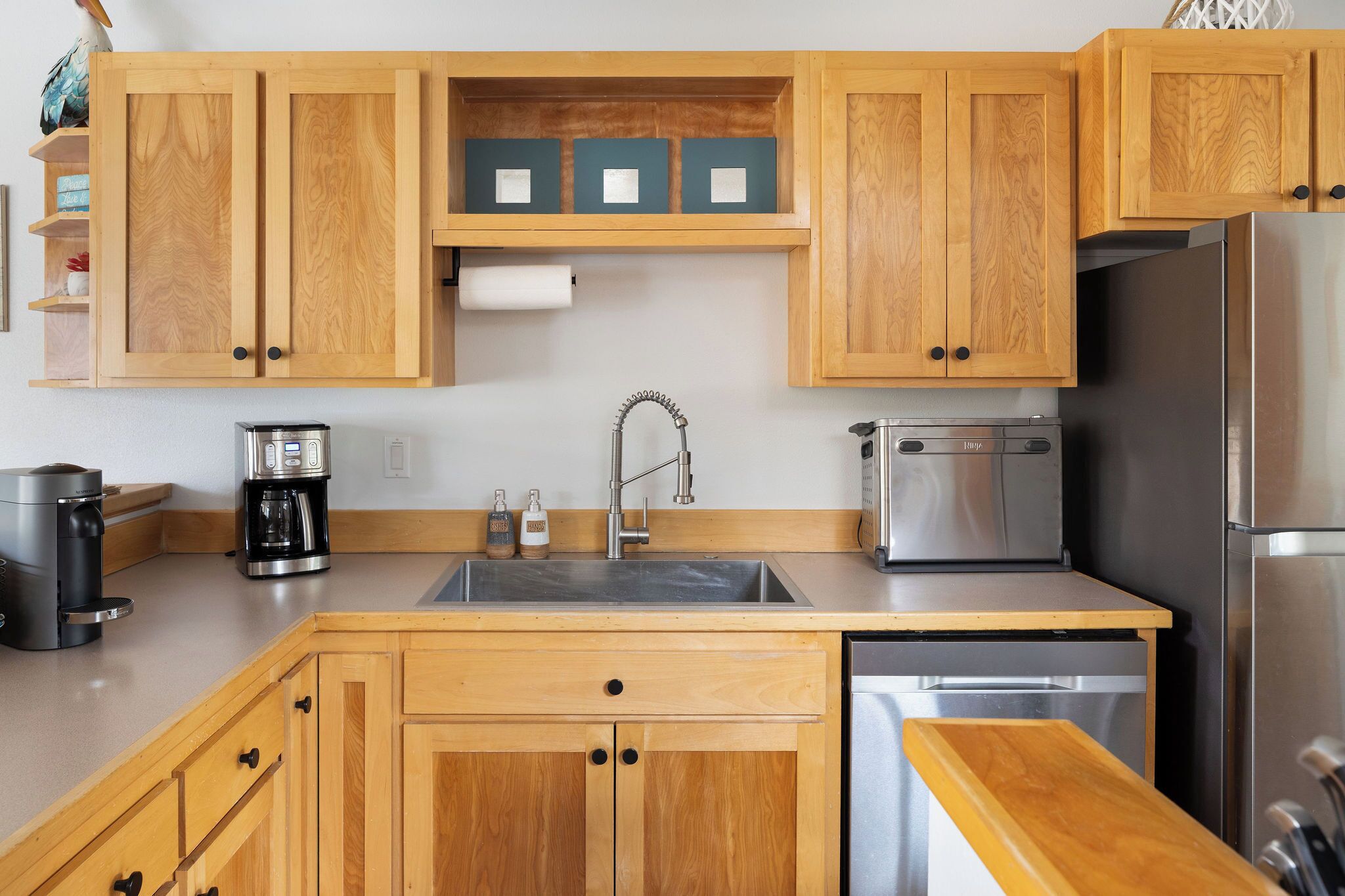 A kitchen with wooden cabinets, a stainless steel sink, a coffee maker, a toaster, and a dishwasher.