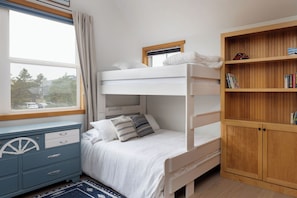 A bunk bed with a window, a desk with drawers, and a bookshelf.