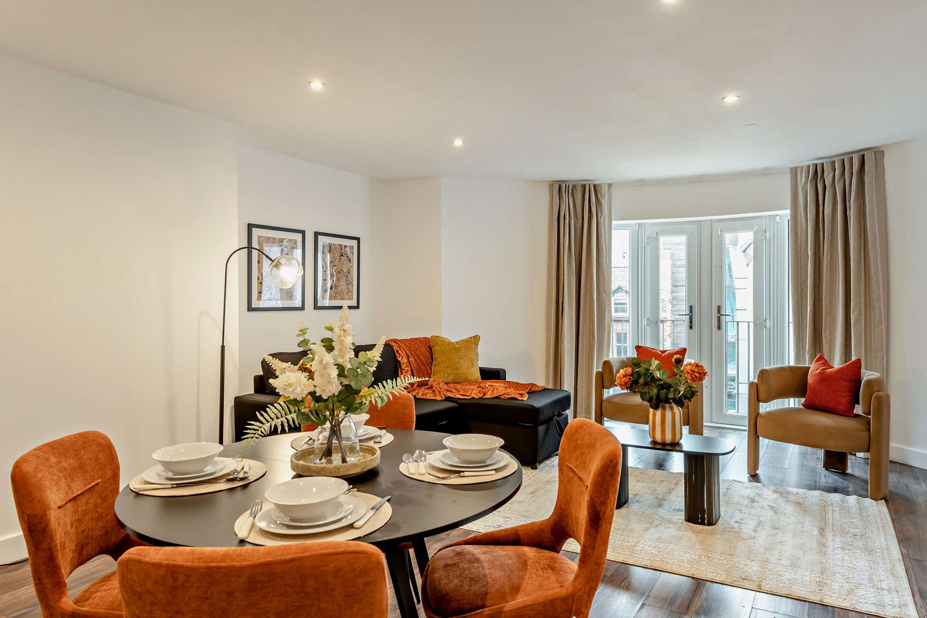 A modern living room with a dining area, featuring a round table set for four, a sofa, and a coffee table with decorative items.