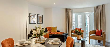 A modern living room with a dining area, featuring a round table set for four, a sofa, and a coffee table with decorative items.