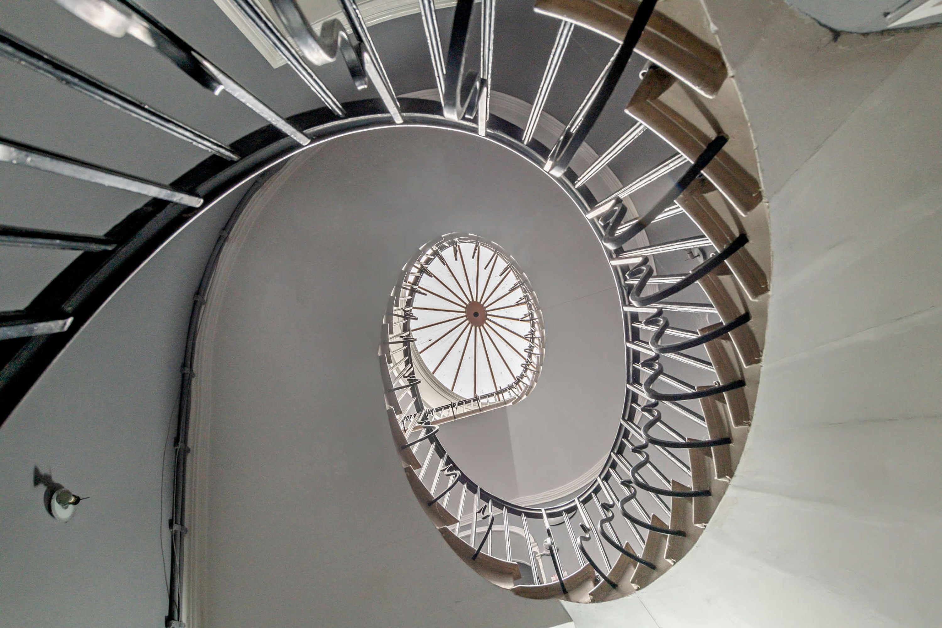 Un escalier en colimaçon doté d’un motif circulaire central et de rampes en métal.