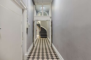 Ein schmaler Korridor mit Schachbrettmuster-Boden, der zu einer Treppe führt.